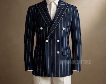 Puede incluir: Una americana azul marino de doble botonadura con finas rayas blancas, seis botones blancos y dos bolsillos delanteros. La americana se combina con una camisa blanca y pantalones blancos. El texto "AMANQUEATTIRE" es visible.
