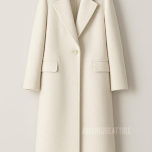 May include: A long, off-white coat with a classic design. It features a notched lapel, a single-button closure, and two front pockets. The coat is made of a soft, textured fabric and has a tailored fit. The text "AMANIQUEATTIRE" is visible on the lower right.
