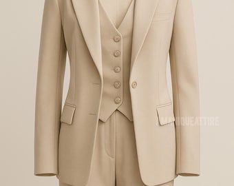 May include: A beige three-piece suit on a mannequin. The suit comprises a blazer with two pockets, a waistcoat with five buttons, and matching trousers. The suit is tailored in a classic style, suitable for formal events. The suit is a neutral beige colour.