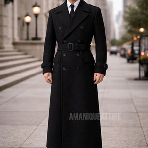 May include: A long, black double-breasted coat with a belt, worn over a white shirt and black tie. The coat has a classic design with a long length and is worn with black dress shoes. The text "AMANIQUE ATTIRE" is visible.
