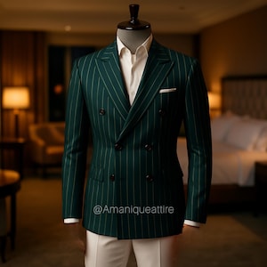 Puede incluir: Un traje cruzado verde oscuro con finas rayas blancas verticales. El traje se exhibe en un maniquí, combinado con una camisa blanca y pantalones blancos. El traje tiene botones marrones oscuros y un pañuelo blanco. El texto "@Amaniqueattire" es visible.