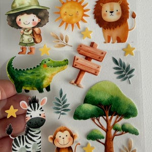 Könnte beinhalten: Ein Bogen mit Rubbelstickern zum Thema Safari. Die Aufkleber zeigen eine lächelnde Sonne, einen Löwen, ein Zebra, einen Affen, ein Krokodil, ein Mädchen in Safari-Outfit, einen Baum und ein Wegweiser. Die Aufkleber sind farbenfroh und skurril.