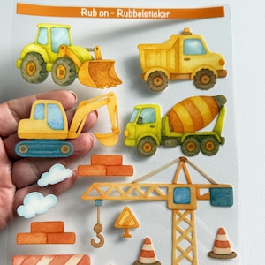 Könnte beinhalten: Ein Bogen mit Rubbelstickern, die Baustellenfahrzeuge im Aquarellstil zeigen, darunter ein gelber Traktor, ein Muldenkipper, ein Bagger, ein Betonmischer, ein Kran, Verkehrskegel, Ziegelstapel, Wolken und eine Absperrung mit Text.