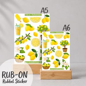 Könnte beinhalten: Zwei Bögen mit Rubbelstickern, beschriftet mit A5 und A6, mit gelben Zitronenmotiven, darunter ganze Zitronen, Zitronenscheiben, ein Zitronenbäumchen im Topf, ein Glas Limonade, ein Eis am Stiel und weiße Blüten, mit dem Text www.musselintraum.de.
