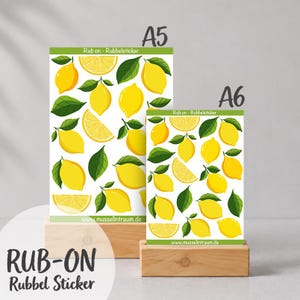 Könnte beinhalten: Zwei Bögen mit Rubbelstickern, die gelbe Zitronenillustrationen und grüne Blätter auf weißem Hintergrund zeigen. Die Bögen sind mit A5 und A6 beschriftet, mit dem Text Rub on - Rubbelsticker und musselintraum.de am unteren Rand.