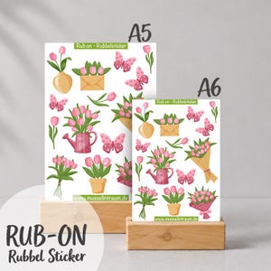Könnte beinhalten: Zwei Bögen mit Rubbelstickern, beschriftet mit A5 und A6, mit Motiven von rosa Tulpen in Vasen, Gießkannen, Umschlägen und rosa Schmetterlingen. Die Bögen enthalten den Text Rub on - Rubbelsticker und www.musselintraum.de.