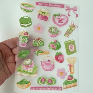 Könnte beinhalten: Ein transparenter Bogen mit Bügelbildern, der verschiedene Matcha-Illustrationen zeigt, darunter Schalen, ein Glas, ein Herz mit dem Text COOL GIRLS DRINK MATCHA, ein Buch mit dem Text JUST A MATCHA GIRL, eine Teekanne und ein Besen in Rosa und Grün.