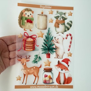 Könnte beinhalten: Ein transparenter Bogen mit Bügelbildern, der weihnachtliche Motive wie Igel, Waschbär, Eisbär, Reh, Fuchs, Kerze, Kekse, Zuckerstange, Sterne und einen kleinen Tannenbaum zeigt, mit dem Text Bügelbilder am oberen Rand.