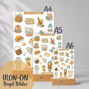 Könnte beinhalten: Drei Bögen mit Bügelbildern in den Größen A4, A5 und A6 mit herbstlichen Motiven wie Kürbissen, Zimtschnecken, einer Katze im Korb, einer Strickjacke, einem Croissant, einer Laterne, einem Corgi und einer Person im Wintermantel.
