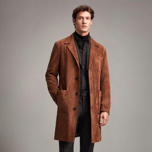 May include: A brown suede coat with a classic design. The coat features a notched lapel, two front pockets, and a three-button closure. The model is wearing a black turtleneck and a patterned shirt underneath.