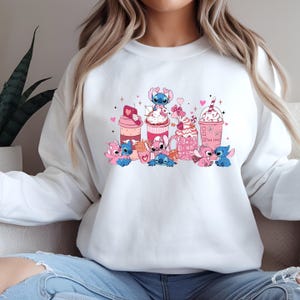 May include: White sweatshirt featuring a colorful graphic of the character Stitch with various pink and red beverages and snacks. The design includes hearts and the words "True Love". The sweatshirt is a casual, comfortable style.