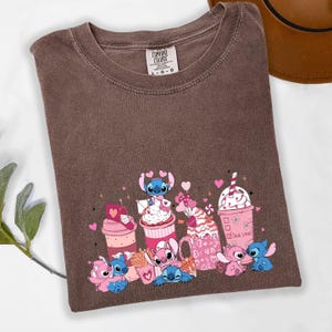 May include: Brown t-shirt with a crew neck and a graphic featuring cartoon characters and pink beverages. The graphic includes the text "True Love" and various heart shapes. The shirt is labeled "Comfort Colors".