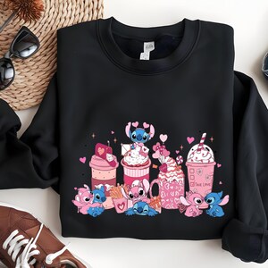 May include: Black sweatshirt featuring a colorful graphic of cartoon characters and various pink and white desserts. The design includes hearts and the words "True Love". The sweatshirt is folded on a white surface.