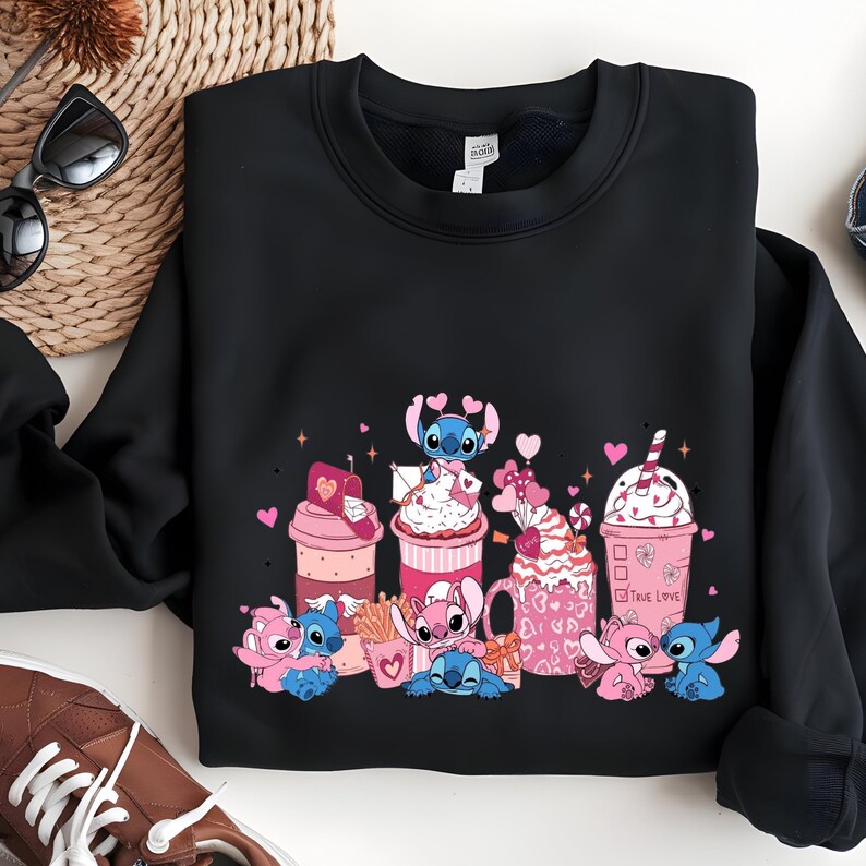 May include: Black sweatshirt featuring a colorful graphic of cartoon characters and various pink and white desserts. The design includes hearts and the words "True Love". The sweatshirt is folded on a white surface.