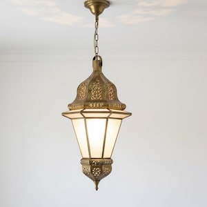 May include: Ornate brass pendant light fixture with a decorative filigree design. The light has a white, frosted glass shade and hangs from a chain. The fixture is suspended from a white ceiling.