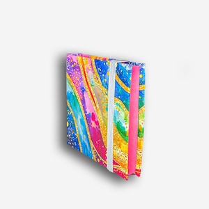 May include: A small, colorful notebook with a gold glitter design and a pink elastic closure. The cover features abstract swirls of blue, pink, green, and yellow.