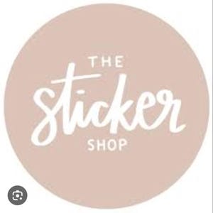May include: A round sticker with a light brown background. The words "THE Sticker SHOP" are written in white, cursive font. The sticker is likely for use on products or packaging.