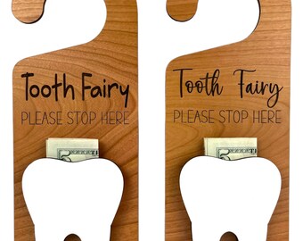 May include: Two wooden tooth fairy door hangers with a slot for a tooth and money. Each hanger has the text "Tooth Fairy Please Stop Here" in black.
