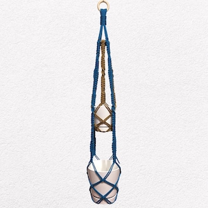 May include: A macrame plant hanger with a wooden ring at the top. The hanger is made of blue and brown rope, holding two white ceramic pots. The pots are empty, ready for plants.