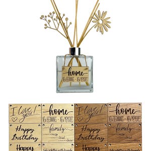 Puede incluir: Un difusor de vidrio transparente con varillas de caña y una flor de madera. La botella tiene una etiqueta dorada que dice "home". Debajo hay placas de madera con frases como "I love you" y "Happy Birthday".