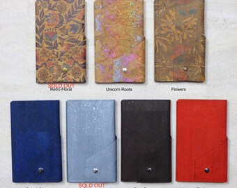 May include: Eight different phone cases made of cork. The cases are in various colors and patterns, including floral, red, blue, brown, and silver. The cases have a flap that folds over the top of the phone. The text "SOLD OUT" appears on two of the cases.