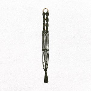 May include: A dark green macrame plant hanger with a wooden ring at the top and a tassel at the bottom. The hanger features a woven design with wooden beads. This decorative item is designed to suspend a plant pot.