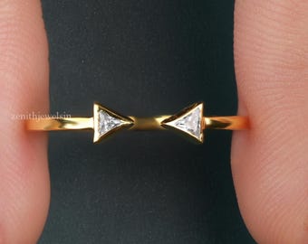 Op de afbeelding: Een gouden ring met twee kleine, heldere, driehoekig geslepen stenen in een strikvormige opstelling. De ringband is dun en gepolijst, met de tekst Zenith Jewels Luxury in Every Detail zichtbaar in de rechterbenedenhoek van de afbeelding.