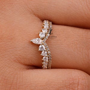 Puede incluir: Un anillo dorado con un diseño curvo, engastado con numerosas piedras preciosas transparentes. El anillo se muestra en una mano, destacando sus intrincados detalles y brillo. Las piedras preciosas están dispuestas en un patrón delicado, creando un aspecto sofisticado. El anillo es una joya.