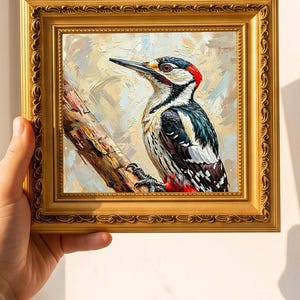 May include: A square oil painting of a woodpecker perched on a tree branch, featuring visible brushstrokes in shades of black, white, and red. The artwork is encased in an ornate, metallic gold frame with intricate decorative carvings along the edges.