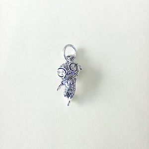 May include: A silver pendant in the form of a stylised insect. The pendant features large, round eyes with clear stones and is detailed with smaller stones. It has a loop at the top for a chain, suitable for jewellery.