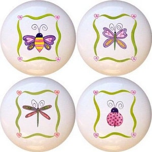 May include: Four white ceramic knobs with green and pink accents. Each knob features a different insect design: a bee, a butterfly, a dragonfly, and a ladybug.