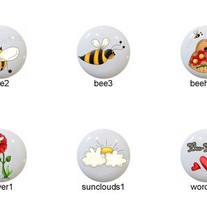 May include: Set of 10 ceramic knobs featuring various bee and flower designs. The knobs are white with colorful painted details. The designs include bees, flowers, a beehive, and a sun with clouds. One knob features the text "You Are My Sunshine".