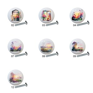 May include: Twelve ceramic cabinet knobs with watercolor-style images of landscapes and windows. Each knob is white with a different image, including a window with flowers, a sunset over a lake, and a field of wildflowers.