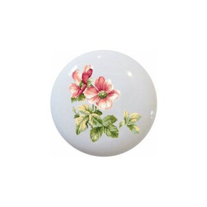 May include: A white ceramic cabinet knob with a floral design. The flowers are pink and red with green and yellow leaves. The knob is round and has a glossy finish.