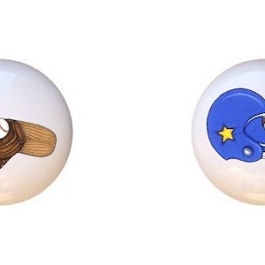 May include: Two ceramic knobs with sports-themed designs. The first knob features a baseball bat, glove, and ball. The second knob features a blue football helmet and a brown football.