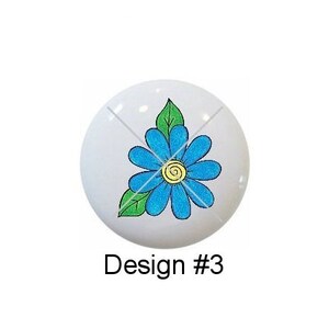 May include: Five round ceramic tiles with different floral and butterfly designs. The designs include a pink flower with green leaves, a blue butterfly with green and yellow accents, a blue flower with green leaves, a purple flower with green leaves, and a pink butterfly with green, yellow, and blue accents.