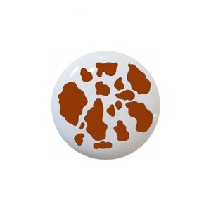 May include: A white ceramic knob with a brown cow print design.