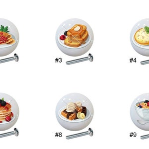 May include: Nine different ceramic cabinet knobs with images of various breakfast foods, including pancakes, waffles, French toast, and crepes. Each knob has a silver screw.