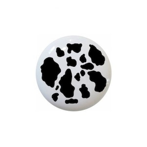 May include: A white ceramic button with a black cow print design.