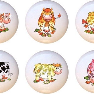May include: Six ceramic knobs with different cow designs. Each knob features a white background with a cartoon cow with different colored spots. The cows are all smiling and have different expressions.
