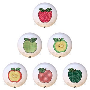 May include: Six ceramic apple drawer knobs with different designs. The knobs are white with a red, green, or red and green apple design. The apples have a plaid or school-themed pattern. The knobs are labeled with numbers 1 through 6.