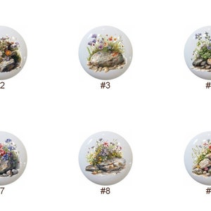 May include: Ten round ceramic tiles with a white background and a painted image of a small cluster of rocks with wildflowers growing on top.