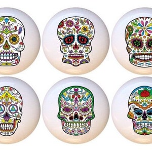 May include: Six white ceramic knobs with colorful Day of the Dead sugar skull designs. Each knob features a different skull design with intricate floral patterns and bright colors.