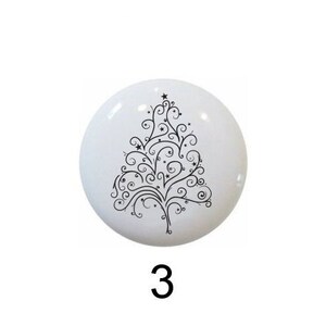 May include: Five different Christmas tree designs on white ceramic knobs. The designs include a green tree with ornaments and a star, a green tree with a star, a black and white stylized tree, a green tree with red ribbon, and a brown pine cone with green pine needles.