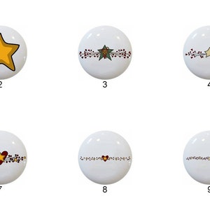 May include: Ten white ceramic knobs with different Christmas-themed designs. The designs include stars, hearts, and holly.