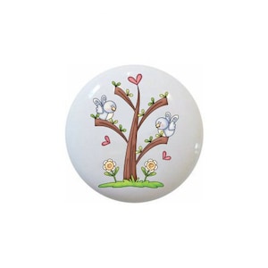 May include: A ceramic knob with a blue and brown tree with two blue birds and pink hearts on a white background.