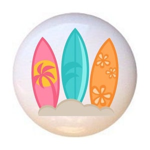 May include: Three colorful surfboards with designs, standing upright in the sand. The surfboards are pink, blue, and orange.