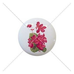 May include: A white ceramic knob with a pink flower design. The flower is a cluster of pink blossoms with green leaves.