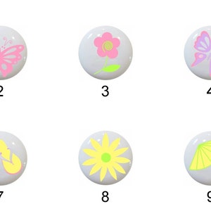 May include: Nine ceramic knobs with different designs, including a palm tree, butterfly, flower, and umbrella. The knobs are white with colorful designs.