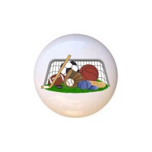May include: A white ceramic knob with a colorful illustration of various sports equipment, including a soccer ball, basketball, baseball, hockey stick, and a baseball bat, all inside a soccer goal.